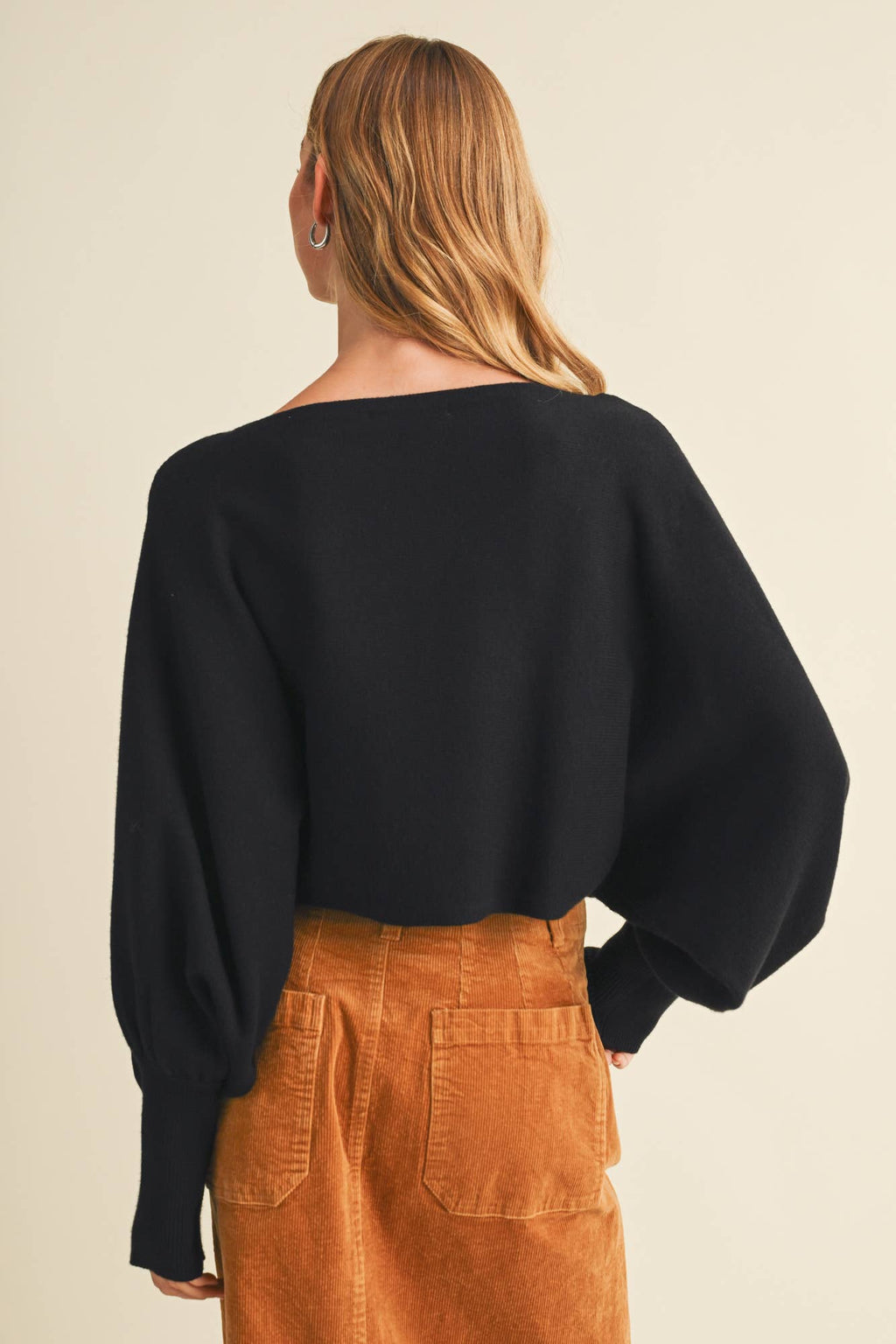 Black dolman pullover back view with wide sleeves over brown pants.
