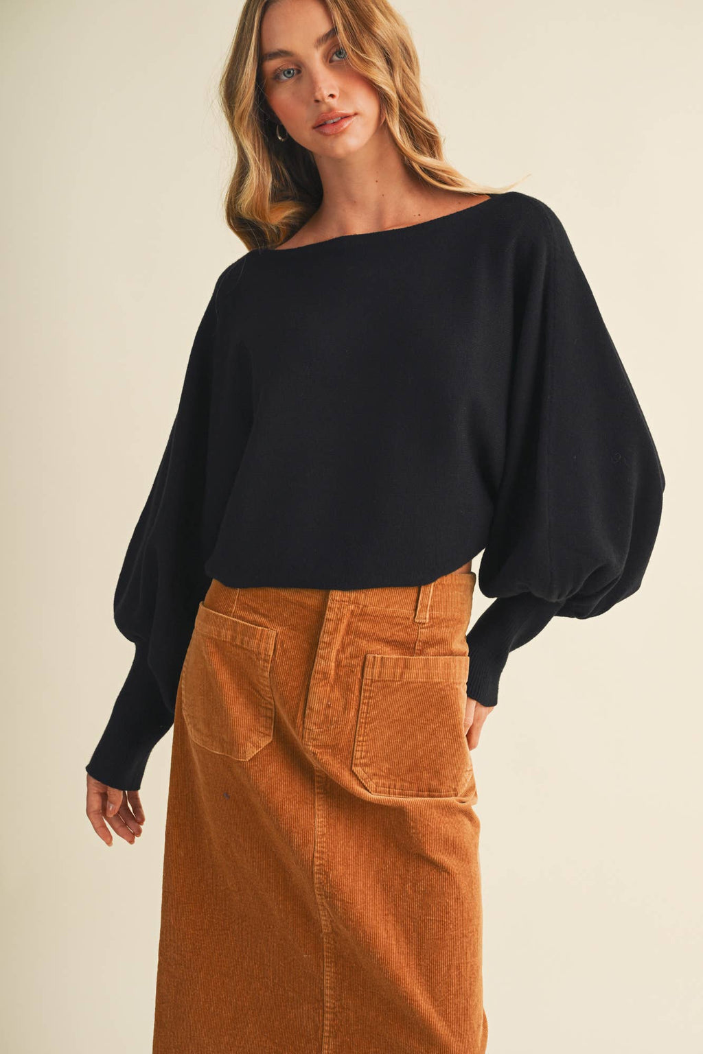 Black dolman pullover with bateau neckline and oversized sleeves, tucked over brown pants.