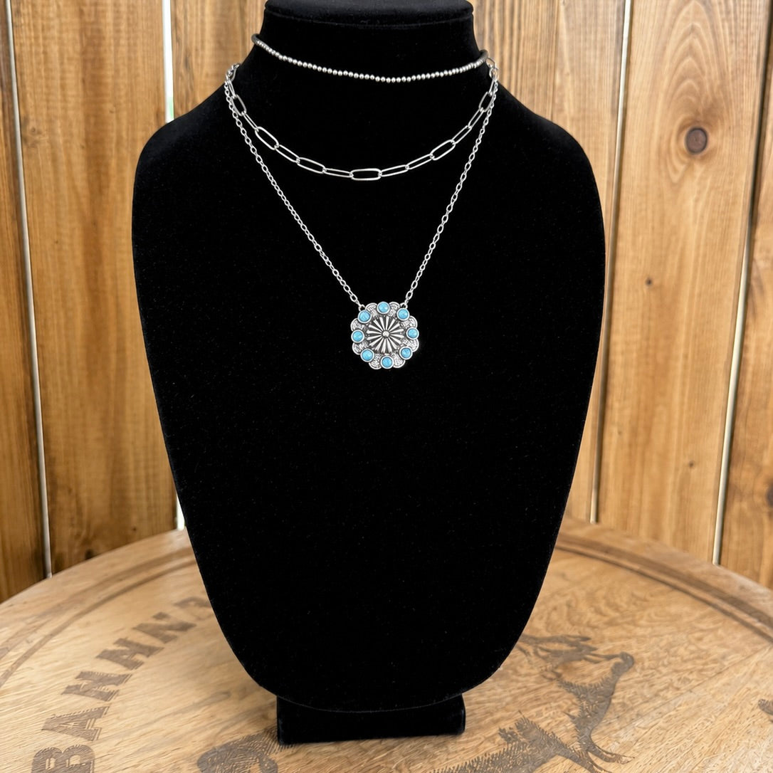 Layered western necklace on bust: silver chain choker and turquoise flower pendant
