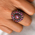 Purple and pink gemstone halo ring with round center and silver-toned prongs