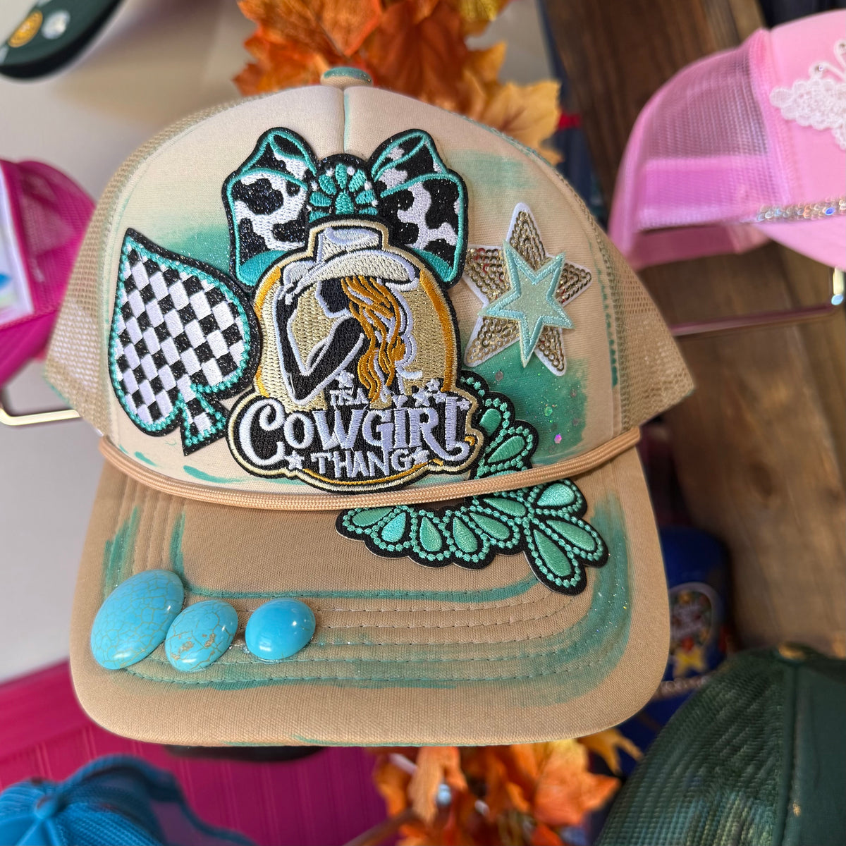 Beige trucker hat with embroidered cowgirl graphic, checkered accents, and teal star patch