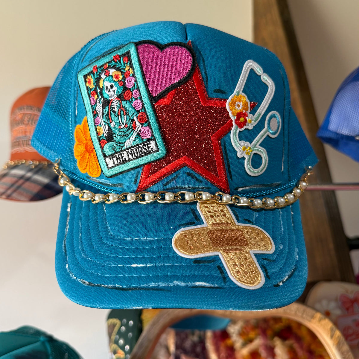 Blue trucker hat with embroidered nurse patch, red star, and gold chain trim