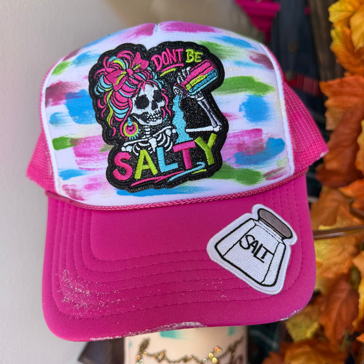 Pink trucker hat with embroidered skull and rose graphic, “DON’T BE SALTY”.
