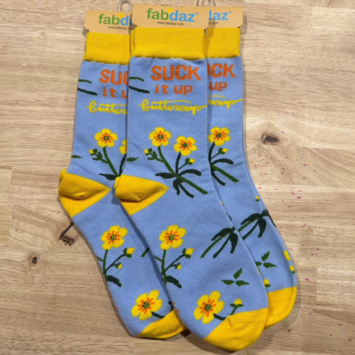 Funny socks with light blue background, yellow flowers, and text 'Suck it up Buttercup'.