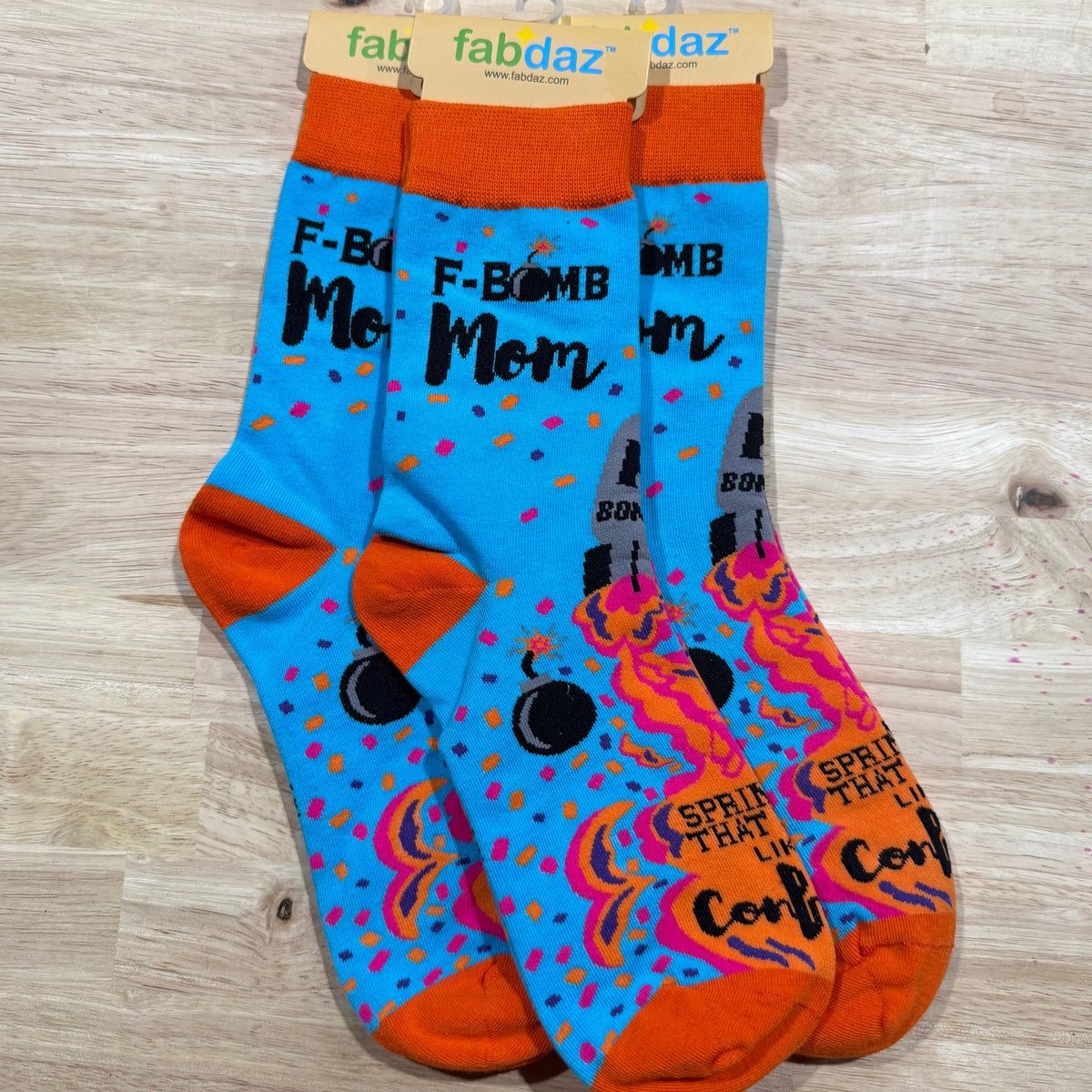 Orange and blue crew socks with “F*CK BOMB MOM” text and colorful blast graphics