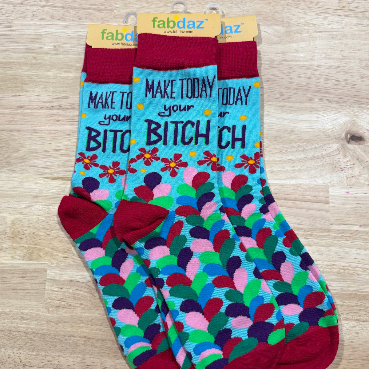 Colorful dot-pattern adult novelty socks with “Make today your…” profanity-style text