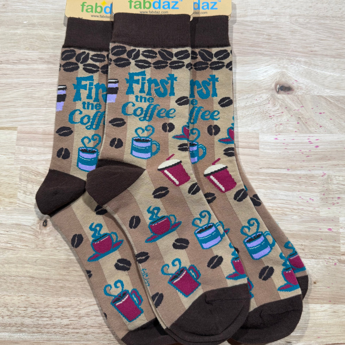 Funny socks with coffee cup and heart pattern on taupe, dark toes, and 'First the Coffee'.