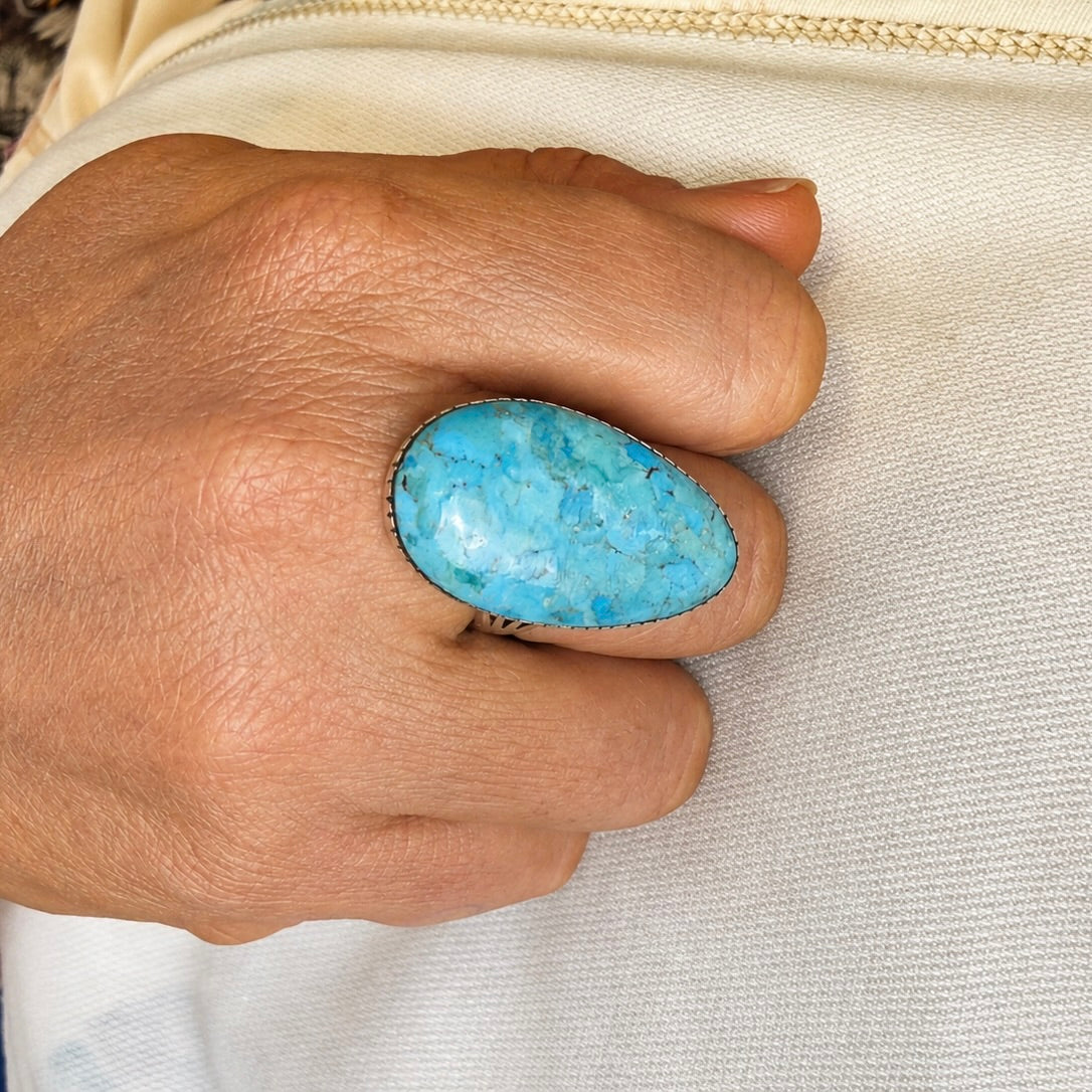 Turquoise oval gemstone ring with dark metal bezel on finger